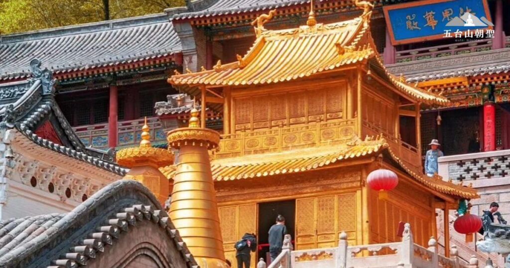 這張圖片展示了五台山華嚴寺內著名的殊像寶殿，金碧輝煌的建築在陽光下閃耀光芒，象徵著佛法的莊嚴與無量光明。金色的塔樓與周圍的漢藏融合建築形成鮮明對比，體現五台山作為佛教聖地的深厚底蘊。紅色燈籠點綴在殿前，增添一絲節慶與祥和的氛圍，吸引無數朝聖者與旅人前來參拜與瞻仰。