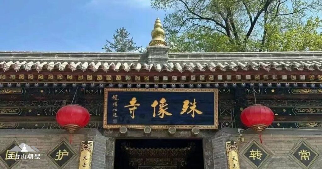 這張圖片展示了五台山殊像寺的正門，門額上書寫「殊像寺」三個大字，象徵著這座寺院的獨特地位。殊像寺位於五台山，是供奉文殊菩薩的主要道場之一，寺內保存著許多珍貴的佛像與經文。寺門兩側懸掛著紅燈籠，增添了一份莊嚴而祥和的氛圍，這裡是許多朝聖者與信眾參拜的重要寺廟之一。