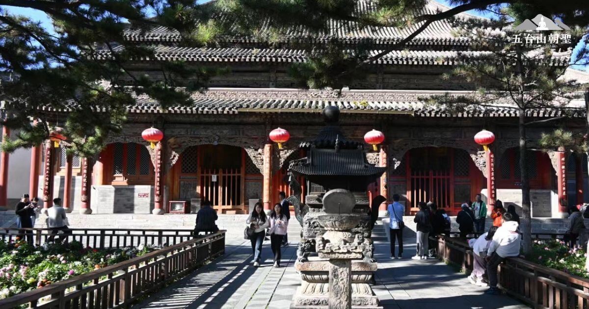 這張照片展示了五台山某座古老寺廟的前庭,庭院內綠樹成蔭,陽光透過松樹灑落,增添了靜謐的氛圍。前方一座大型香爐散發著淡淡的香煙,象徵著信眾的虔誠供奉。木造大殿雕梁畫棟,屋頂層層相疊,展現了古典建築之美。遊客輕聲漫步,感受五台山的莊嚴與寧靜。這裡既是修行者靜心之地,也是旅人探索佛教文化的重要景點。