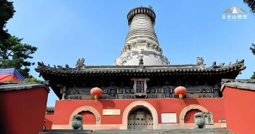 這座雄偉的大白塔矗立在五台山顯通寺內，是該寺最具代表性的佛教建築之一。塔身潔白，呈瓶狀，象徵清淨與智慧，被視為五台山的地標之一。塔前的紅色門樓與懸掛的燈籠增添了莊嚴與祥和的氛圍，而石獅則守護著這座千年佛門聖地，迎接四方來朝的信眾與旅人。