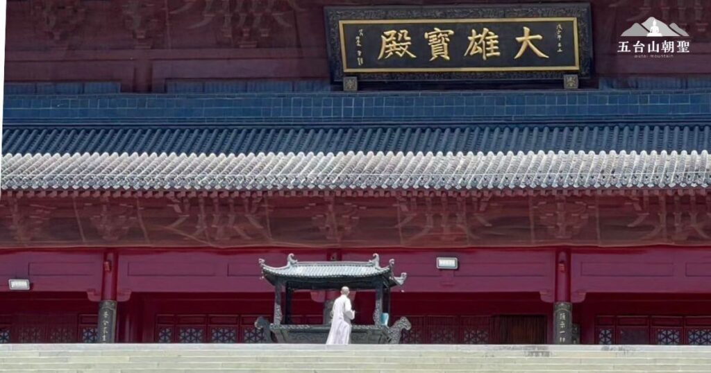 這座大雄寶殿是五台山的重要佛教建築之一，殿宇氣勢恢宏，紅牆黑瓦的設計展現莊嚴氛圍。正殿上方懸掛「大雄寶殿」金字匾額，象徵釋迦牟尼佛的智慧與慈悲。畫面中，一名僧人正在焚香禮拜，展現朝聖者虔誠的修行儀式。這裡是佛教信徒與遊客沉澱心靈、參拜修行的聖地，吸引眾多朝聖者前來敬拜與祈願。