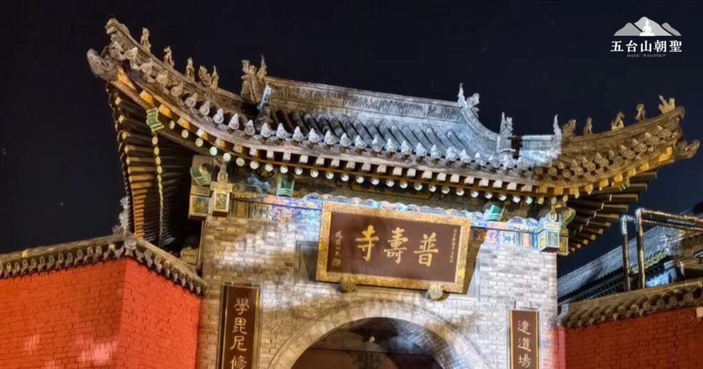 這張照片展現了夜晚的五台山普壽寺大門,寺廟的古建築在燈光照耀下更顯莊嚴肅穆。門額上掛著「普壽寺」的匾額,象徵著普渡眾生、福壽綿延的寓意。紅色磚牆與傳統灰瓦屋頂形成鮮明對比,而精緻的木雕與飛檐讓整體建築更具中國古典美感。夜色之下,天空中的點點星光增添了一份靜謐,為信眾提供了一個沉靜修行與祈願的氛圍。