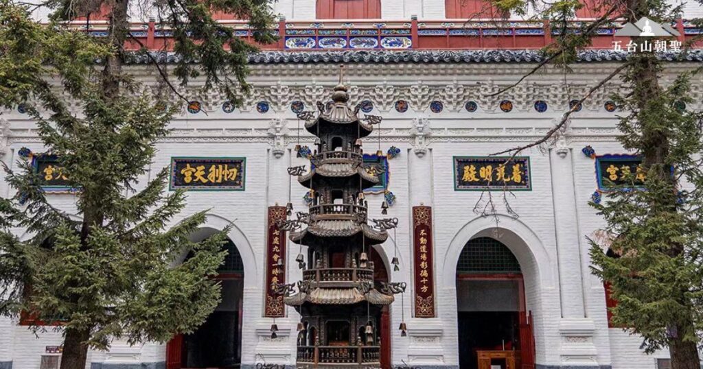 這張圖片展示了五台山一座著名寺院的正門景觀。潔白的牆面鑲嵌著精美的藍色匾額,上書佛教經文,展現莊嚴氛圍。中央矗立著一座精緻的多層香爐,周圍松樹環繞,增添一絲清幽之感。這座佛門聖地不僅是修行者的精神寄託,也吸引無數朝聖者前來祈福、感受五台山的佛法智慧與寧靜氛圍。