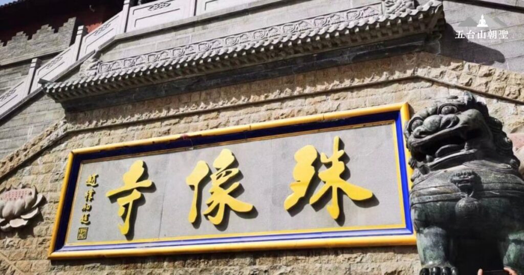 此圖展示五台山殊像寺的正門，門上懸掛著「殊像寺」的金字匾額，周圍建築以石材為主，保留了古樸的風格。右側可見一座威嚴的石獅，象徵守護寺院的神聖力量。該寺院是五台山著名的佛教道場之一，吸引無數信徒與旅人前來朝聖與參拜。