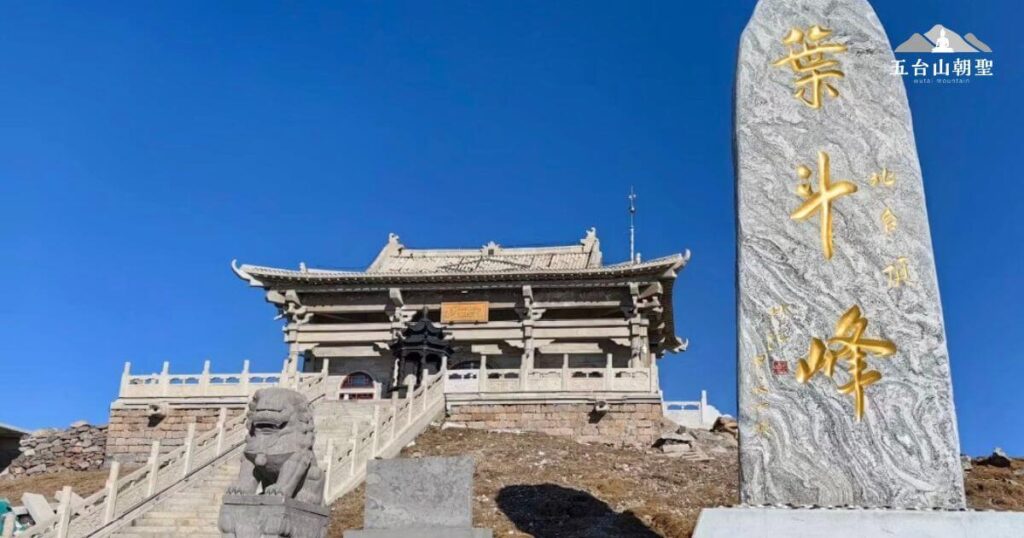 這張照片展示了五台山北台（葉鬥峰）的標誌性石碑，石碑上刻有「葉鬥峰」四個金色大字，象徵著北台在五台山五大主峰中的崇高地位。在石碑旁，一座古樸的寺廟矗立在山頂，階梯蜿蜒而上，兩旁有石獅守護，顯示出莊嚴肅穆的氛圍。藍天映襯下，整個景色更加壯麗，展現出佛教聖地的寧靜與神聖，這裡是許多信眾與登山者朝拜的重要地點。