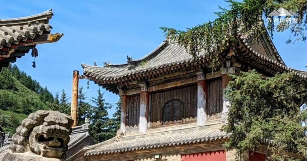 這張圖片展示了五台山碧山寺（Bishan Temple）的一角，擁有傳統中式木結構建築，屋簷精雕細琢，古色古香。畫面中的石獅象徵著守護與威嚴，而遠處的青山與綠樹則襯托出寺廟的靜謐與祥和。碧山寺是五台山著名的佛教寺院之一，為修行者與朝聖者提供一個沉澱心靈的場所。