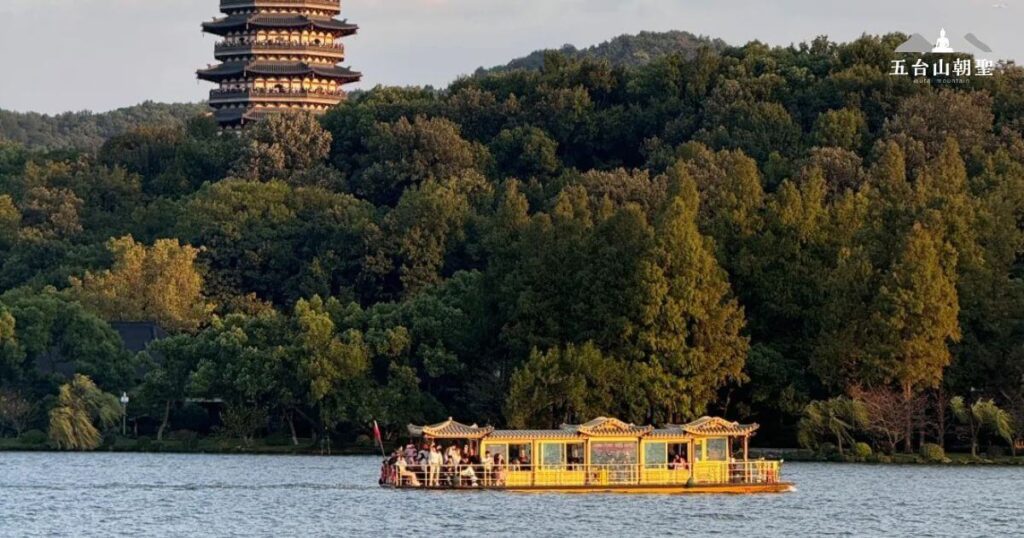 這張圖片展示了在浙江杭州的西湖（West Lake）上進行的船遊。船隻載著遊客，穿行於湖水之中，遠處是著名的雷峰塔。西湖的景色四季如畫，是中國最具代表性的旅遊景點之一。湖岸兩側的翠綠樹木與山脈相依，為遊客提供了優美的自然景觀。
