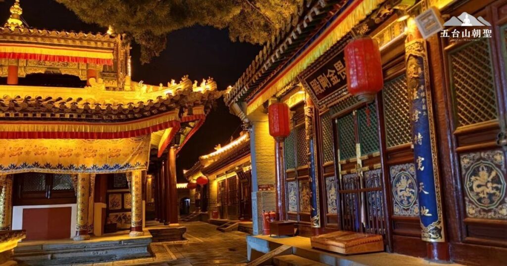 這張圖片展示了**五台山（Wutai Mountain）**的佛教寺廟在夜晚燈光映照下的壯麗景象。金黃色的燈光勾勒出屋簷的優雅曲線，精美的建築細節和雕刻在光影間更顯華麗。紅色燈籠點綴於廟宇長廊，營造出莊嚴寧靜的氛圍，突顯寺廟的傳統文化底蘊。畫面中的裝飾與題字展現了佛教的精神內涵，讓人感受到五台山作為佛教聖地的神聖氣息。這張圖片適合用於展示五台山寺廟的夜景魅力，突顯其莊嚴與祥和。