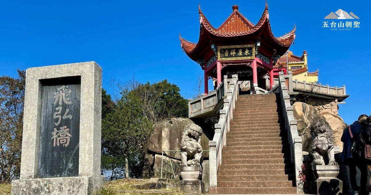 這張圖片展示了東雅禪寺的飛虹橋入口，橋旁有兩座石獅守護，橋上通往一座具有傳統中國風格的寶塔。寶塔屋頂呈現出紅色與金色的搭配，顯得格外醒目，與周圍的自然景觀相得益彰。清澈的藍天與周圍綠樹交織，展現出一種寧靜且神聖的氛圍。