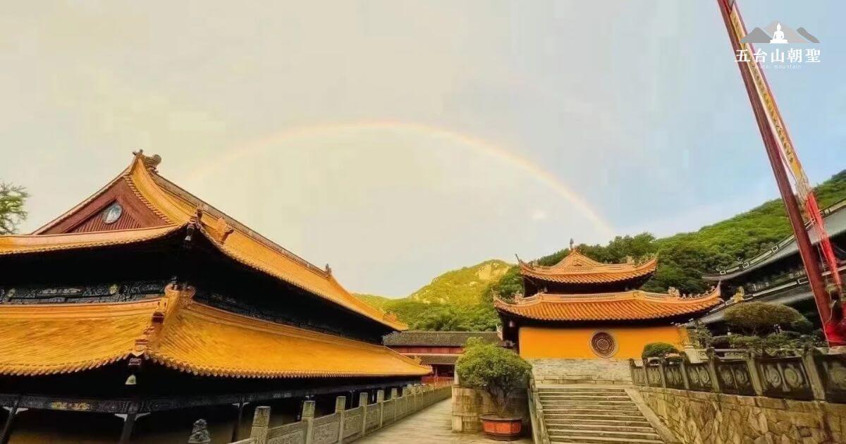 這張圖片展示了中國法雨寺（Fayu Temple）的壯麗景象。寺廟的屋頂呈金黃色，遠處山脈背景與天空的彩虹相映成趣，增添了這個地方的神聖與平靜氛圍。法雨寺是著名的佛教寺廟之一，擁有悠久的歷史與文化背景，是信徒與遊客前來朝聖的重要場所。