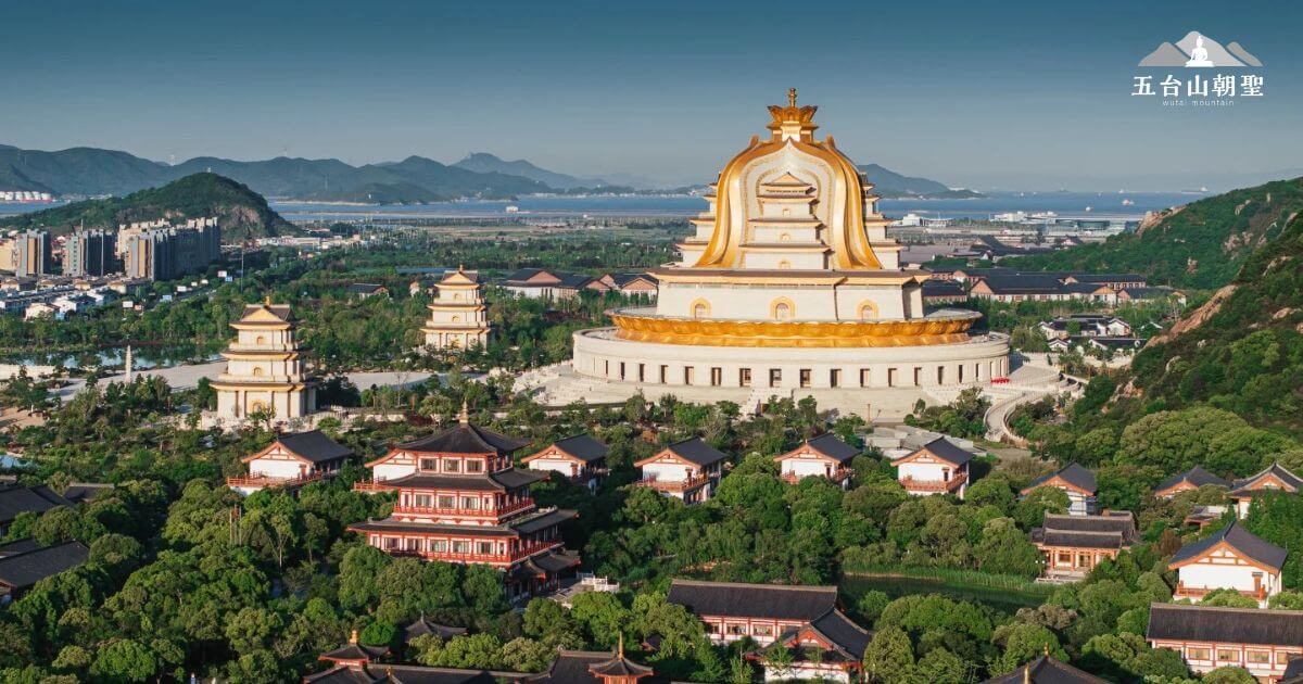 這張圖片展示了壯麗的觀音法界寺廟，位於一片郁郁蔥蔥的綠地中，與遠處的山脈相映成趣。這座宏大的寺廟有著金色的圓頂和精緻的建築結構，周圍環繞著其他低矮的樓閣，展現出濃厚的宗教氛圍。畫面中，寺廟的規模令人印象深刻，與現代城市背景形成鮮明對比，仿佛將神聖與現代生活完美融合。