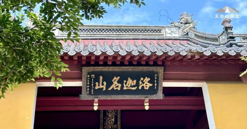 這張圖片展示了羅家山（Luojia Mountain）的入口處，古色古香的大門上方懸掛著「山名洛家」的匾額。山門的設計具有濃厚的中式傳統風格，並搭配著周圍綠意盎然的樹木，營造出寧靜的氛圍。這裡是眾多喜愛登山和尋求心靈平靜的遊客的理想目的地。