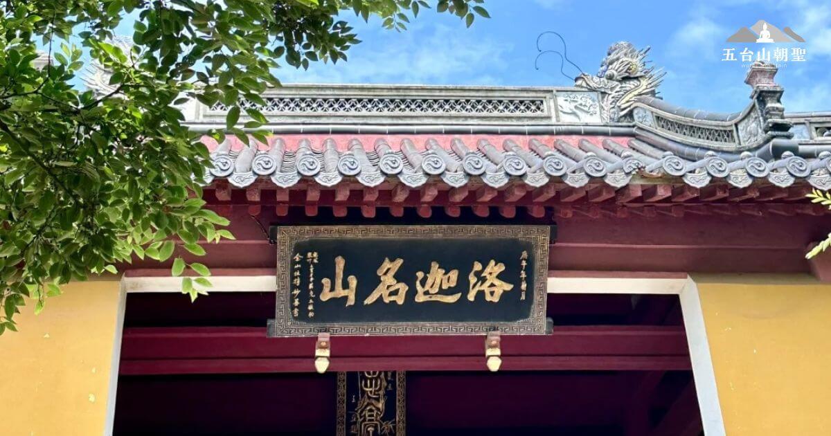 這張圖片展示了羅家山（Luojia Mountain）的入口處，古色古香的大門上方懸掛著「山名洛家」的匾額。山門的設計具有濃厚的中式傳統風格，並搭配著周圍綠意盎然的樹木，營造出寧靜的氛圍。這裡是眾多喜愛登山和尋求心靈平靜的遊客的理想目的地。