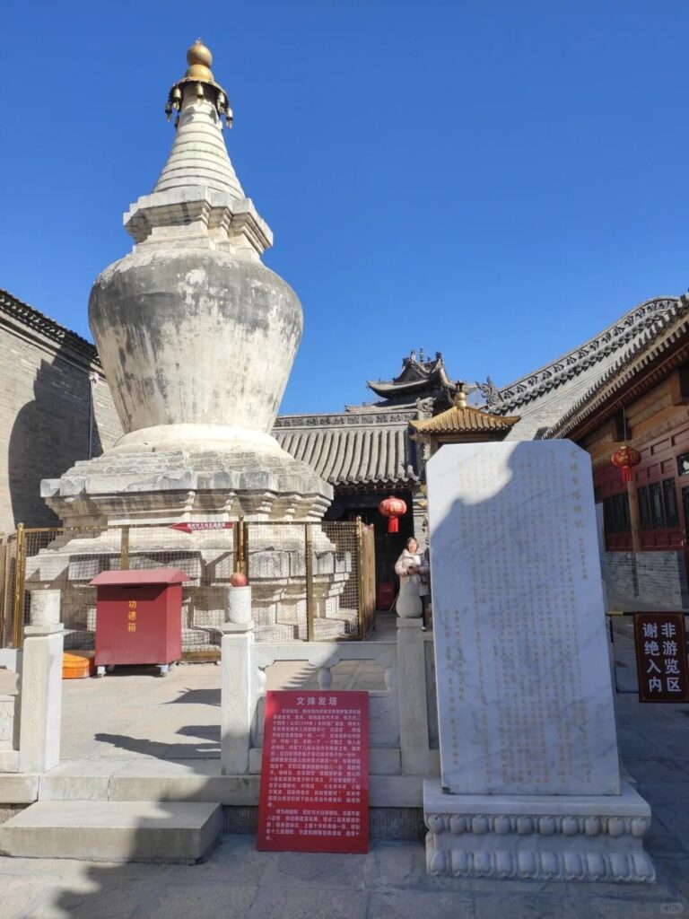 這張圖片展示了位於五台山的文殊菩薩塔,塔身高聳,形狀獨特,擁有明顯的佛教文化象徵。圖片中的石碑提供了關於塔的背景資訊,並有指示牌指示遊客注意進入區域的規範。此塔是五台山的重要文化和宗教景點之一。