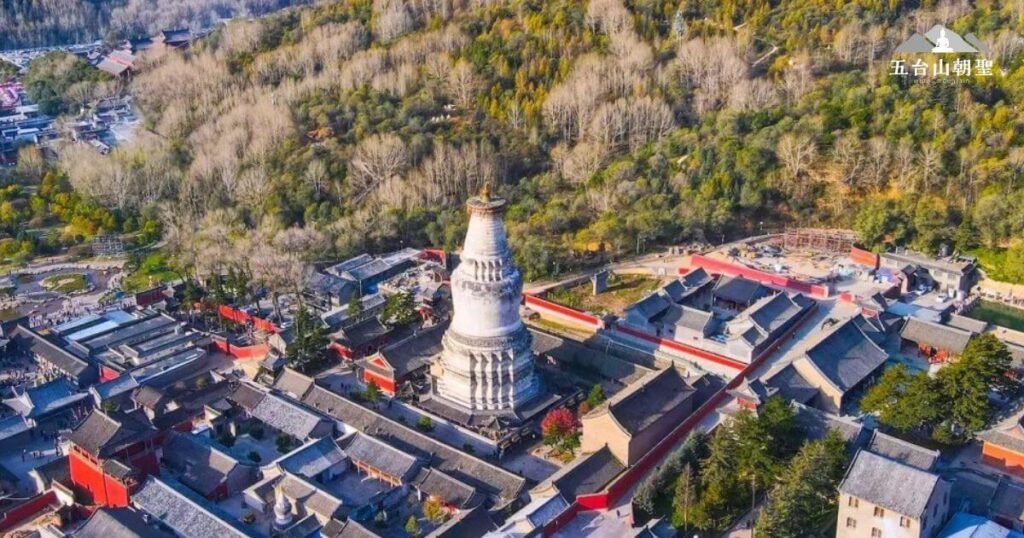 這張圖片展示了五台山的全景，俯瞰著悠久的寺廟建築群和遠處的山脈景色。圖片中的塔樓與寺院周圍的翠綠山脈交織，呈現出一幅和諧的畫面，象徵著五台山的靜謐與神聖。這樣的景色不僅吸引了朝聖者，也成為眾多遊客拍照留念的熱點。這張圖片非常適合用來介紹五台山的自然美景和文化底蘊，激發讀者對五台山之旅的興趣。