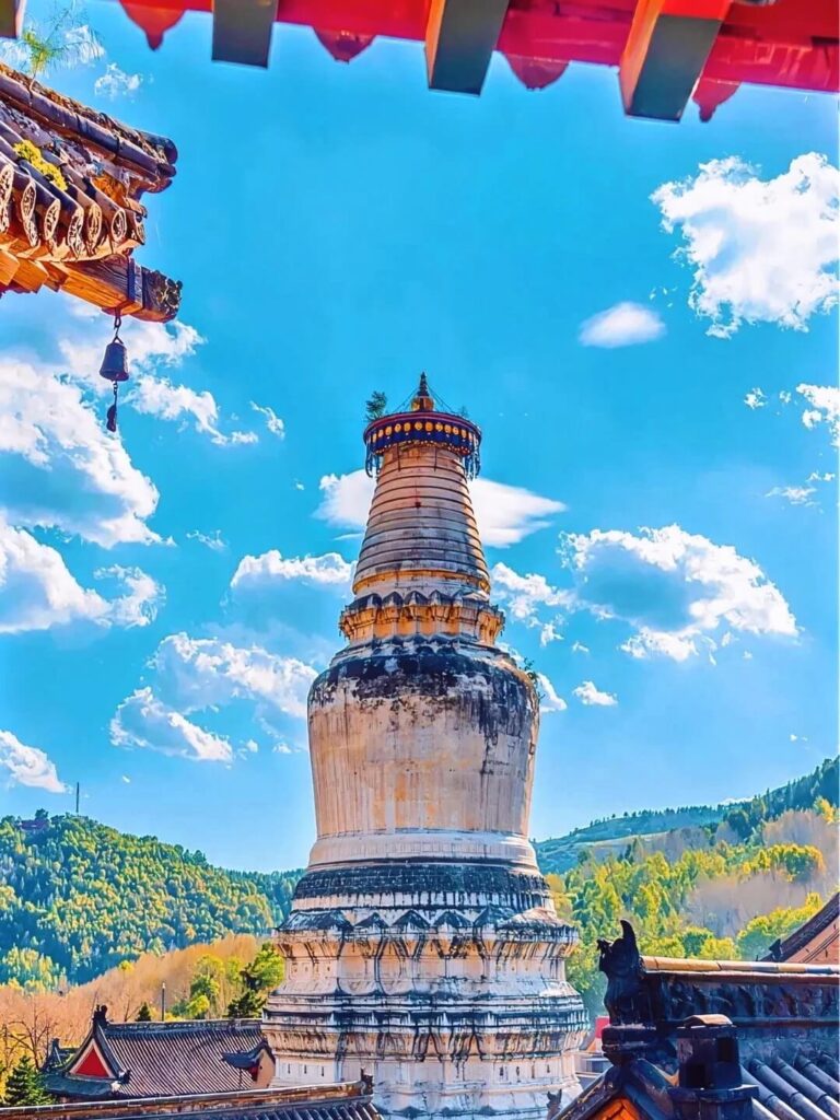 這張圖片展示了五台山的釋迦牟尼舍利塔的壯觀景象，塔身高聳入雲，周圍是蔚藍的天空與翠綠的山脈。塔頂與遠山的景色交織，呈現出一種神聖與和諧的氛圍。舍利塔是佛教信仰的重要象徵，信徒們來此朝聖，感受佛法的力量和心靈的啟發。