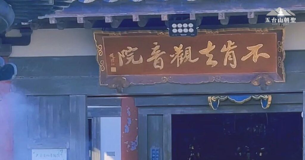 這張照片展示了中國寺廟的入口處，顯示了“拒絕進入觀音院”的標誌，這可能是該地區的宗教場所或某個特定的文化象徵。這個畫面呈現出典型的中式建築風格，金色字體與深色背景形成鮮明對比，周圍環繞著一些虔誠的信徒或遊客，展現出神聖與靜謐的氛圍。
