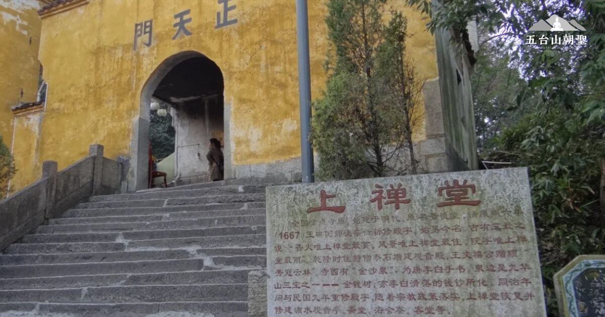 這張圖片顯示了上禪寺（Shangzenji Temple）的入口，寺廟的大門上方寫著「天正門」，搭配古老的建築風格，充滿歷史感。石階的兩側長滿綠意，標牌旁邊的文字介紹了這座寺廟的歷史背景，吸引著每年眾多的信徒和遊客來此朝聖與瞻仰。
