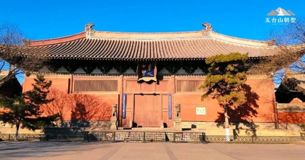 這張照片展示了五台山善化寺的正殿，古樸的紅色牆面與深色屋頂形成鮮明對比，呈現出莊嚴肅穆的氛圍。藍天映襯下，古木掩映，增添了靜謐感。寺門上方懸掛著「善化寺」牌匾，象徵著這座擁有千年歷史的佛教聖地。善化寺作為五台山的重要寺廟之一，承載著豐厚的文化與宗教價值，吸引無數信眾與朝聖者前來參拜，尋求心靈的平靜與啟發。