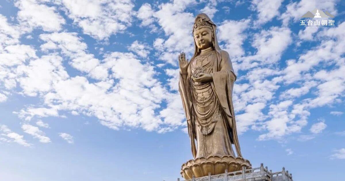 這張照片展示了南海觀音立像（Standing Statue of Guanyin），坐落於海邊，背景是藍天與白雲的廣闊景象。觀音菩薩以慈悲的姿態立於蓮花座上，象徵著佛教的慈悲與救度。這尊高達108米的雕像是世界上最高的觀音雕像之一，吸引了無數朝聖者和遊客前來參拜。