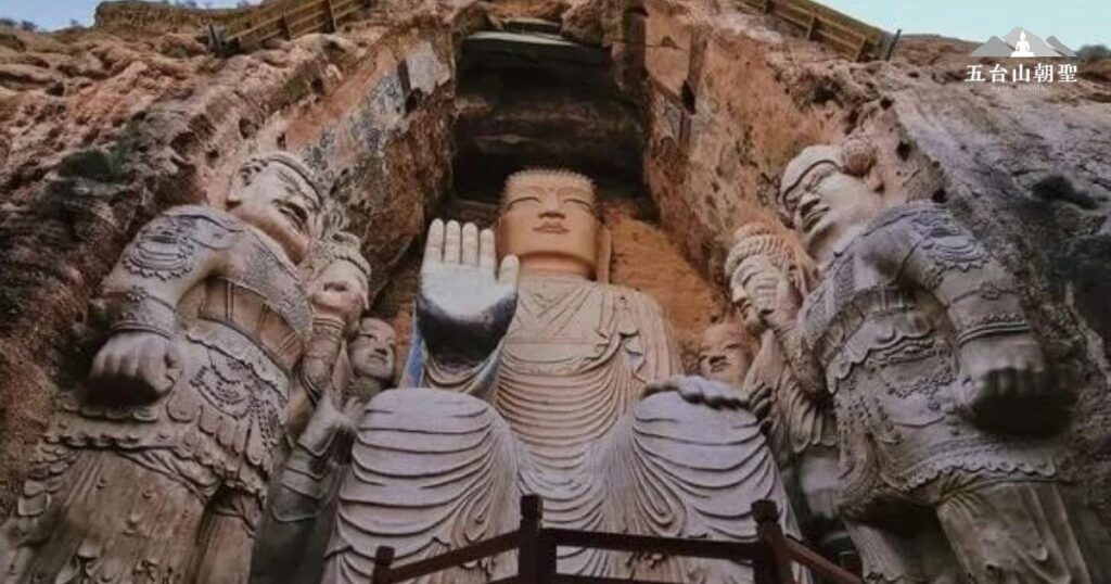 山西太原的天龍山石窟（Tianlongshan Grottoes），該石窟始建於東魏至北齊時期，歷經隋唐擴建，是中國佛教石窟藝術的重要遺產。圖中的巨大佛像位於其中一個主要石窟內，莊嚴端坐，手勢呈現「施無畏印」，象徵佛陀的智慧與庇佑。周圍的護法天王與菩薩雕像姿態生動，展現當時精湛的雕刻技藝。
