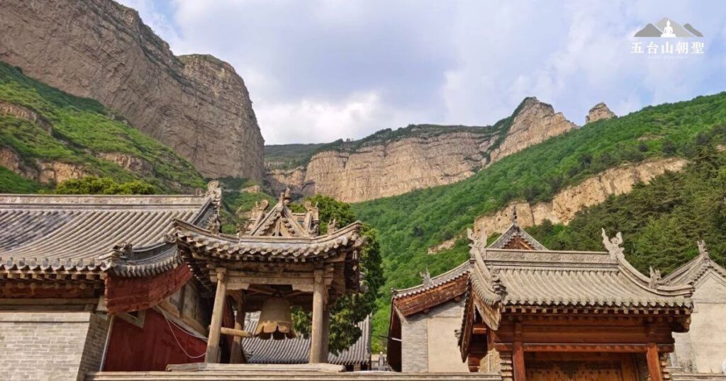 這張圖片展示了五台山(Wutai Mountain)一座古老寺廟的鐘樓,前方懸掛著一口歷史悠久的大鐘,象徵佛教的法音傳播。周圍的傳統中式建築雕刻精美,屋簷飛翹,展現濃厚的佛教文化氛圍。背景則是雄偉的山巒與翠綠的植被,襯托出寺廟的寧靜與莊嚴。這裡是五台山著名的佛教聖地,吸引無數朝聖者與旅人前來參拜與修行。