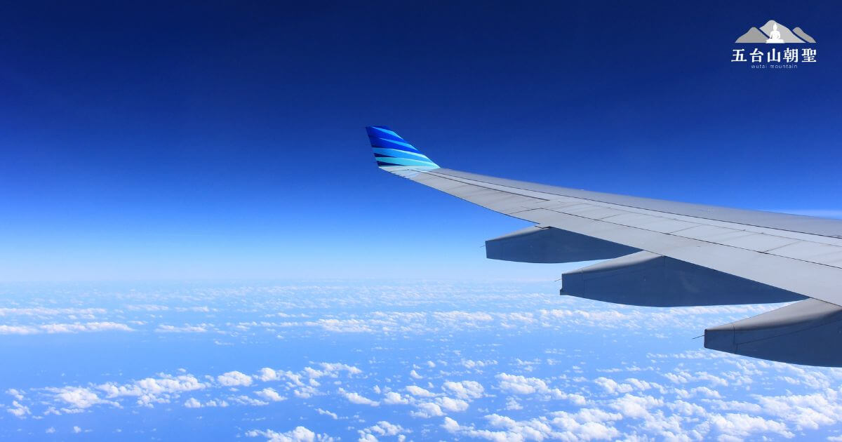 這張圖片拍攝自飛機窗戶,展示了飛機翼與藍天白雲的壯觀景色。飛機的尾翼帶有藍色條紋,與廣闊的天空相互輝映,營造出寧靜且令人嚮往的旅程氛圍。右上角的「五台山朝聖」標誌強調了這趟航班與五台山朝聖之旅的連結,適合作為旅遊行程宣傳,象徵著順利啟程、飛往心靈聖地的意象。