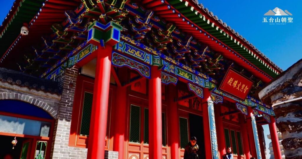 這張圖片展示了五台山南台寺的建築,紅柱、藍綠雕花的斗拱以及屋簷上的精美彩繪,突顯出中國傳統寺院建築的華麗與莊嚴。陽光照耀下,色彩更加鮮明,建築細節一覽無遺,讓人感受到這座寺廟的歷史與文化底蘊。這裡是朝聖者與遊客常來參拜的靈修之地,象徵著智慧與覺悟。