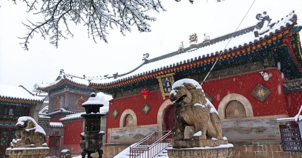 雪中五台山顯通寺，寺前石獅與紅牆屋簷覆蓋白雪，古樸莊嚴